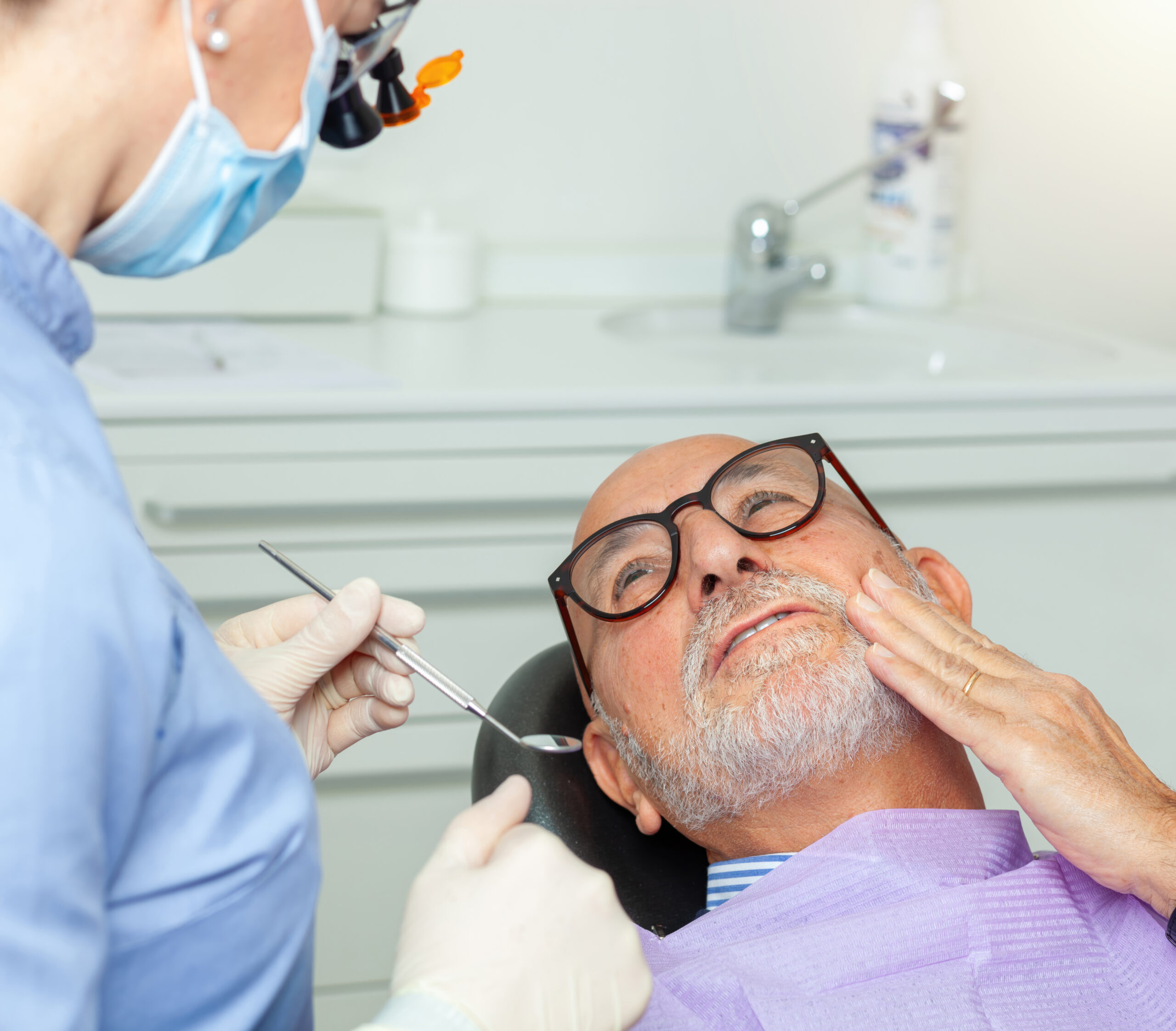 Senior man experiencing toothache during a dental checkup, showing signs of worry while undergoing examination in a clinic