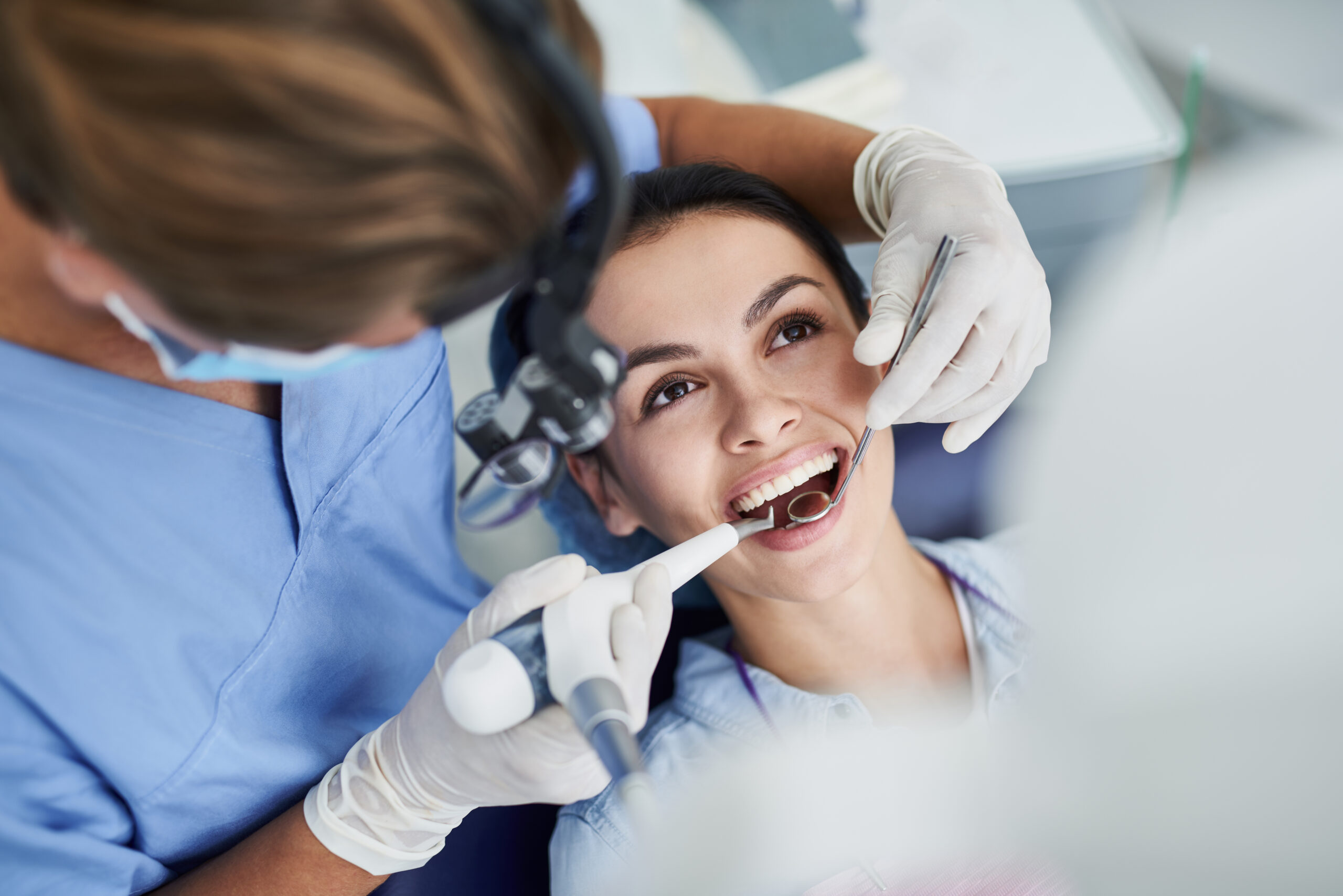 Top view portrait of beautiful lady with opened mouth sitting in dentist chair while stomatologist in sterile gloves doing professional teeth cleaningTop view portrait of beautiful lady with opened mouth sitting in dentist chair while stomatologist in sterile gloves doing professional teeth cleaning