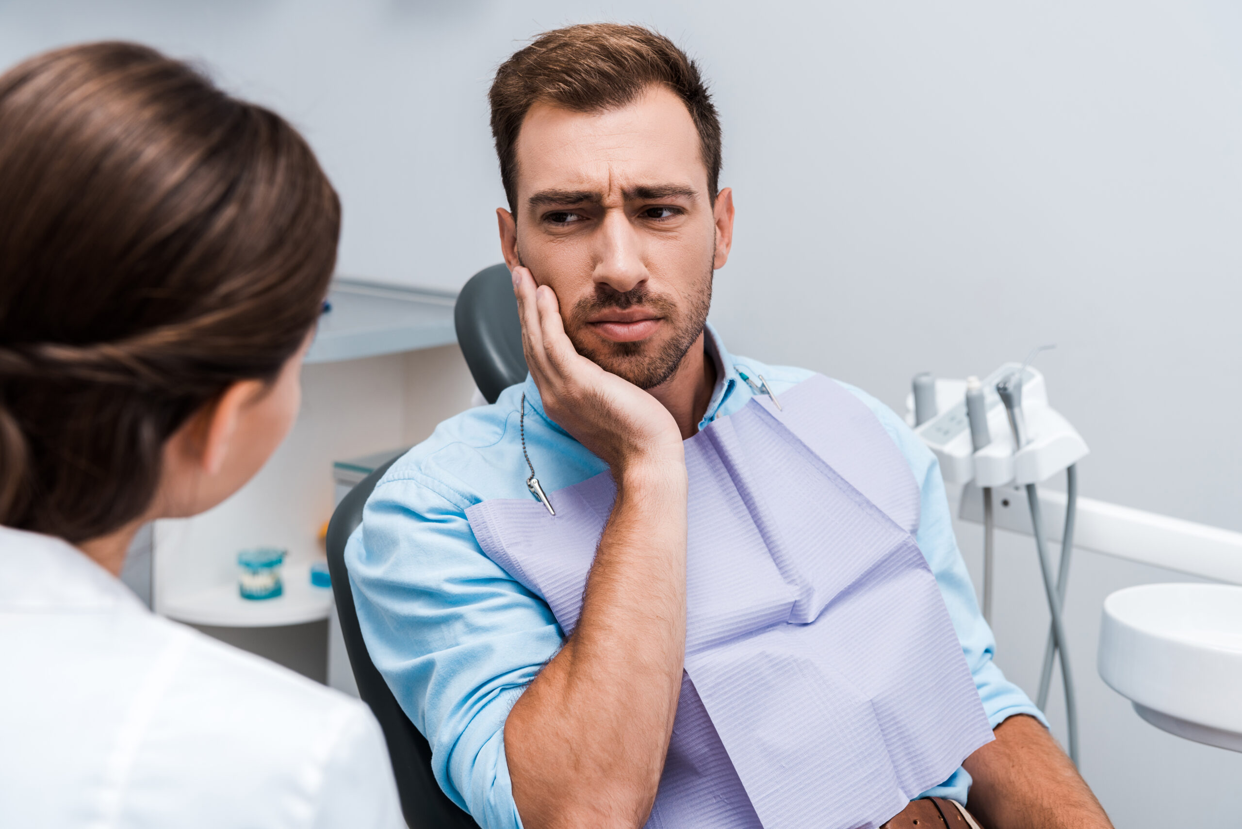 selective focus of upset patient touching face while having toothache near dentist