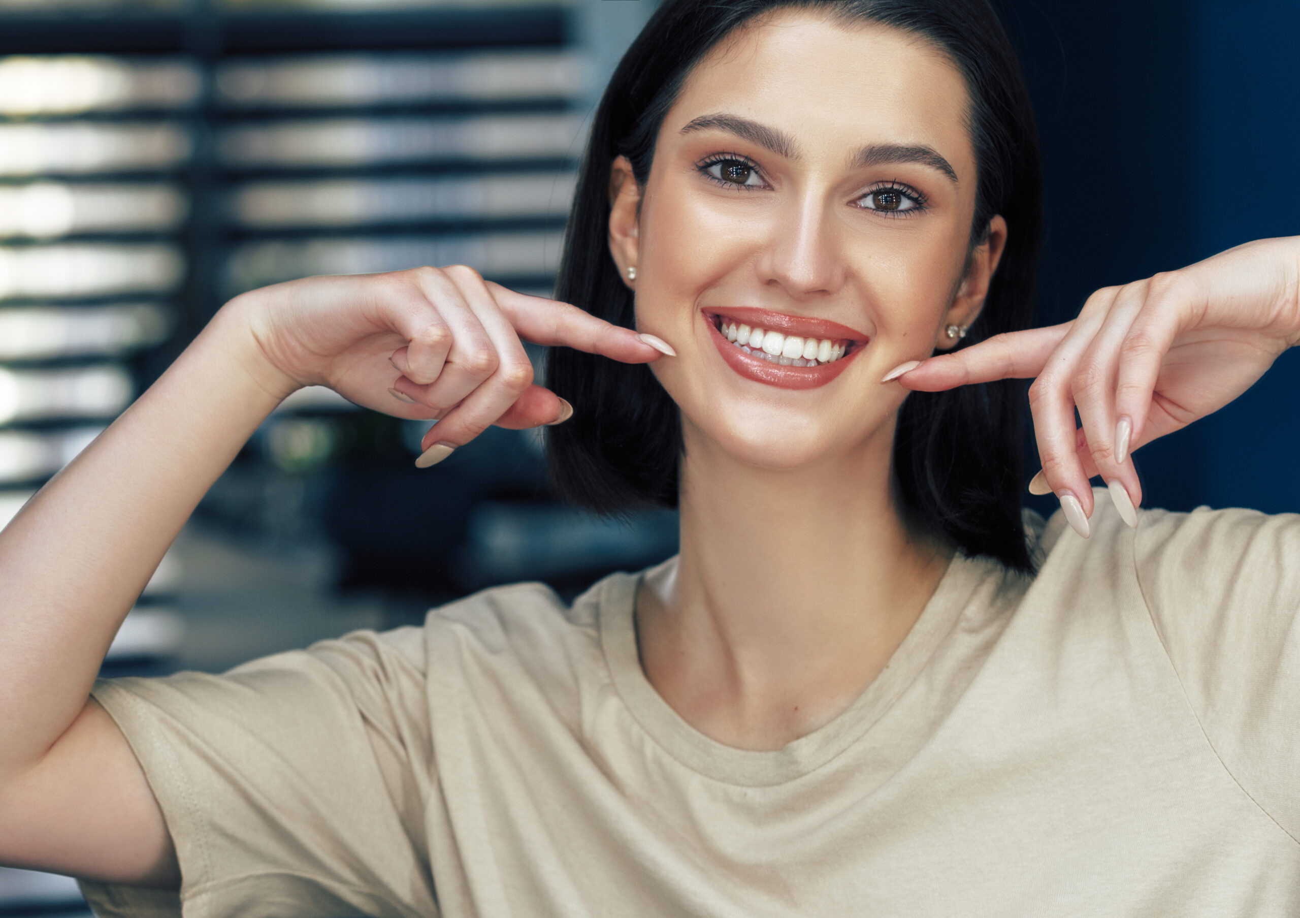 Portrait of a positive attractive girl with natural makeup smiling and showing with index fingers her healthy white teeth. Pretty young woman has joyful expression after makeup.