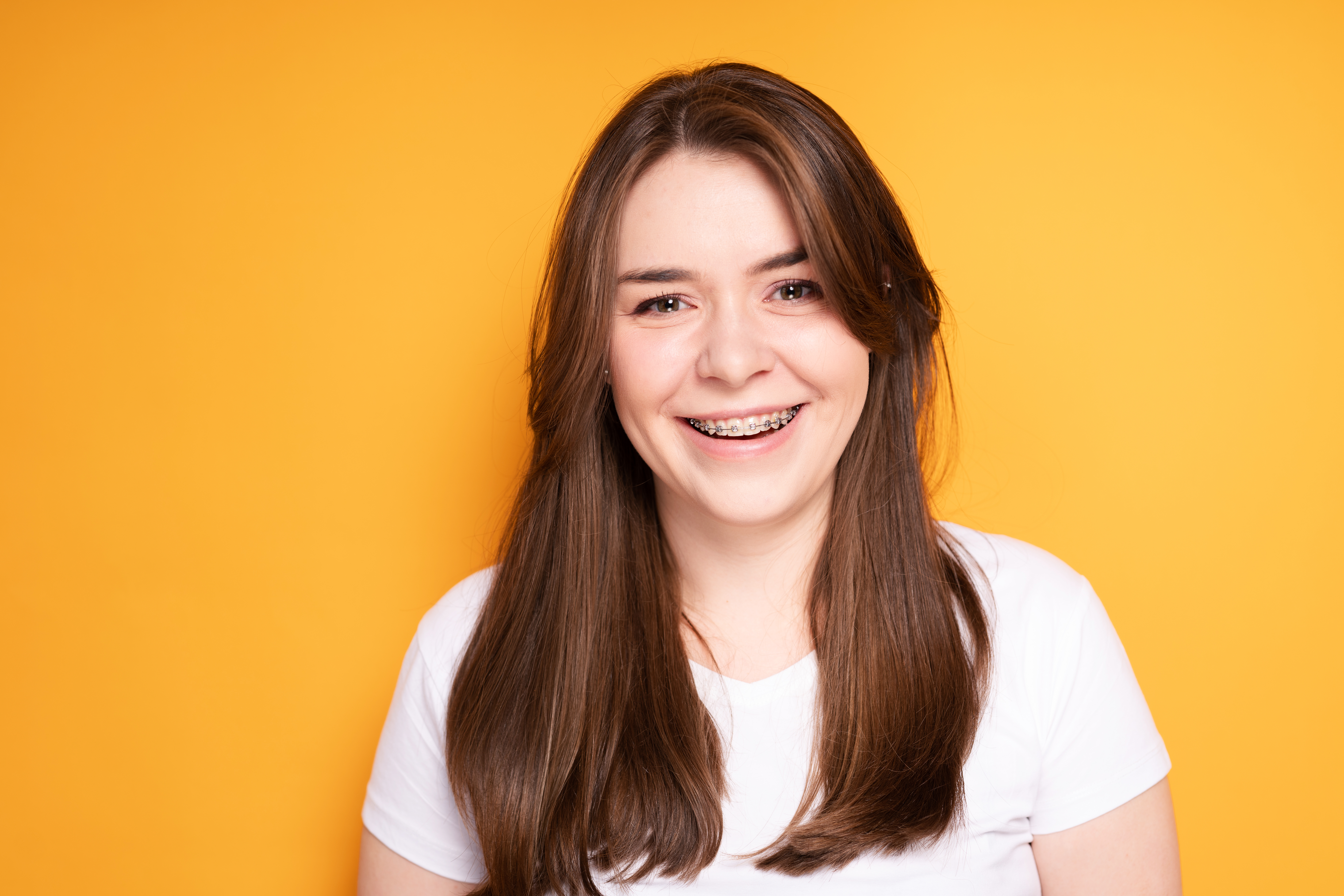 Beautiful brunette with long hair with braces smiling and looking at the camera. High quality photo