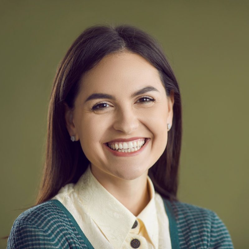 Studio close up portrait of happy smiling good looking woman. Closeup headshot of cheerful confident young girl in smart casual outfit, with pretty face and charming natural smile on green background